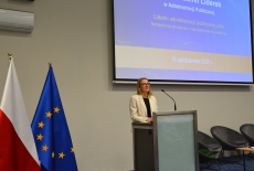 Przy mównicy stoi kobieta i przemawia.