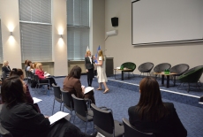 Na środku auli stoja  dwie Panie i przemawiają przed uczestnikami