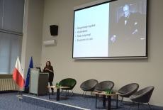 Przy mównicy stoi kobieta i przemawia.