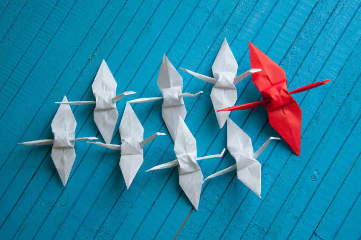 stado ptaków origami, na czele jeden większy czerwony, za nim grupa białych